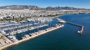 A marina with numerous boats docked, a long pier, and a cityscape with mountains in the background. - Sun-Kissed Sailing Adventure in Islas Sarónicas (Alimos)
