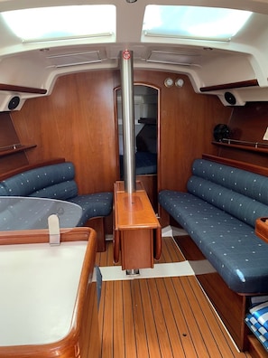 A boat interior with a central table, two blue cushioned seating areas, a vertical pole, and a windowed ceiling. - Sun-Kissed Sailing Adventure in Islas Esporadas (Skiathos)