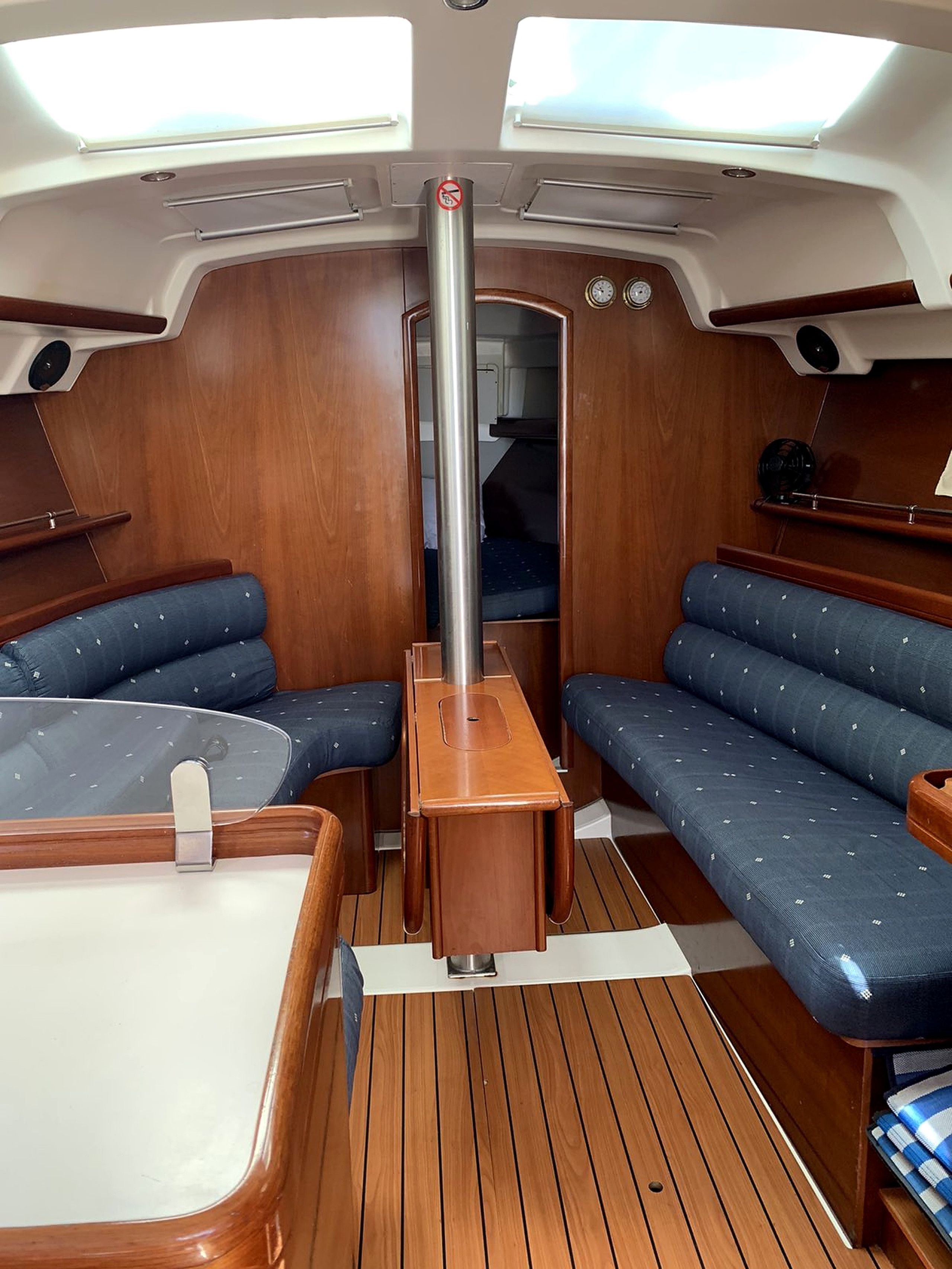 A boat interior with a central table, two seating areas with blue cushions, and a wooden floor.