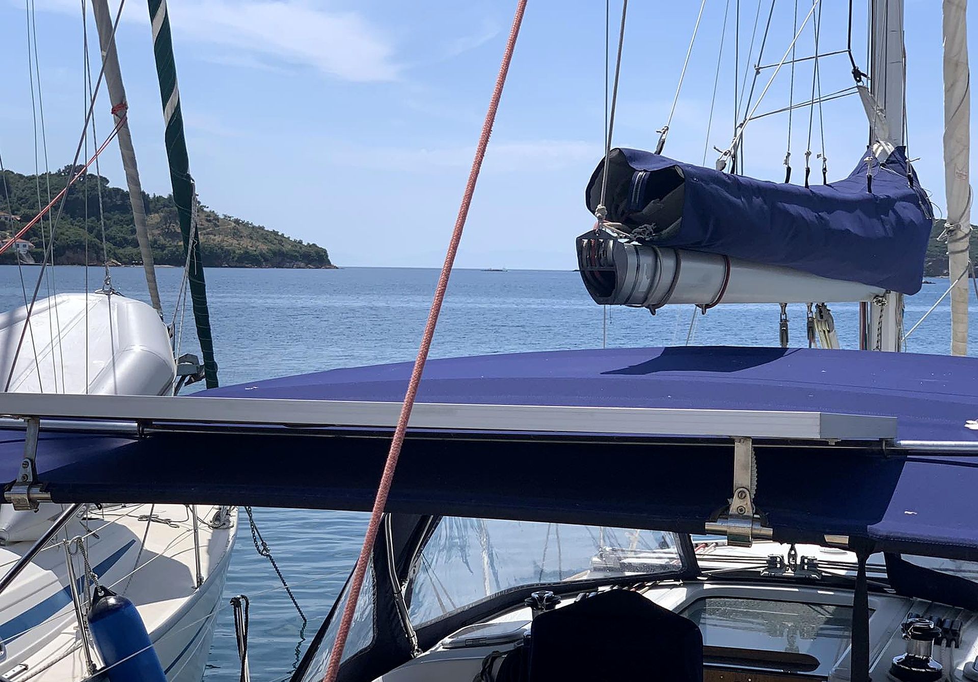 A sailboat with a covered deck, a winch, and a view of the sea and a distant landmass.