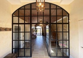 Un pasillo con un amplio arco de entrada, suelo de piedra y una escalera que sube a un nivel superior.
