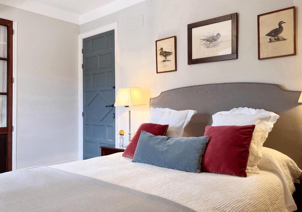 A neatly made bed with pillows, a lamp, and framed pictures on the wall.