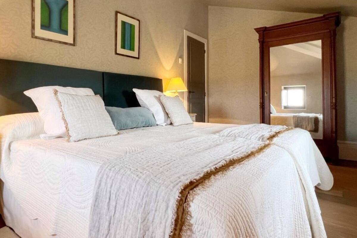A large bed with a headboard, a bedside lamp, and a mirror on the wall.