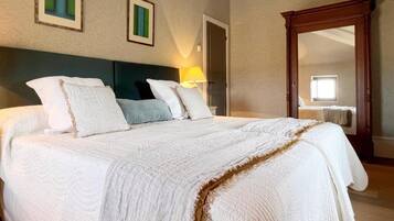 Een groot bed met hoofdeinde, een bedlampje en een spiegel aan de muur.