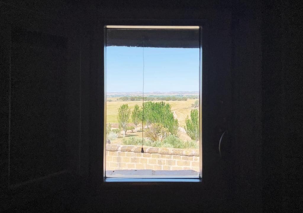 Una ventana con vista a un paisaje, incluyendo árboles y un horizonte lejano.