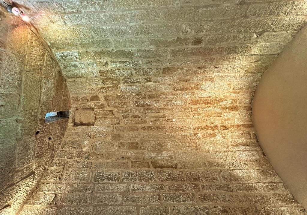 A stone-walled corridor with a narrow passageway and a curved wall on one side.