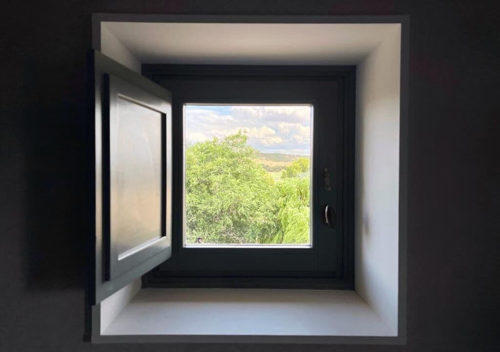Ventana con tragaluz que ofrece vistas a zonas verdes y colinas.