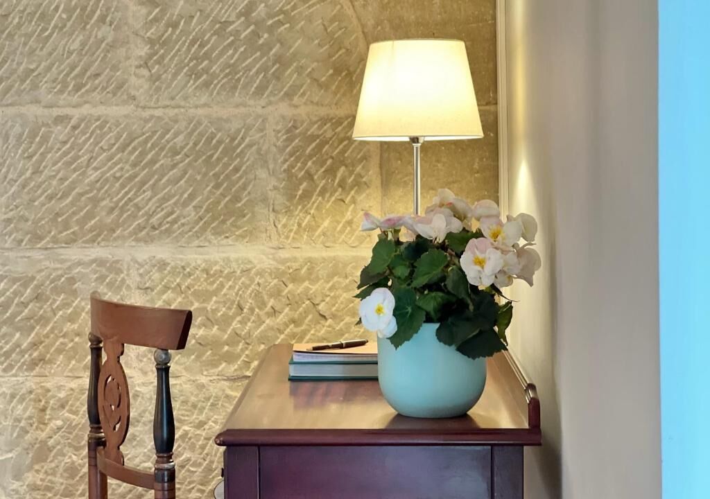 Une chaise en bois, un bureau avec une lampe et un vase rempli de fleurs.
