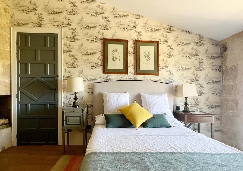 Een slaapkamer met een bed, twee nachtkastjes, een deur en behang met een patroon.