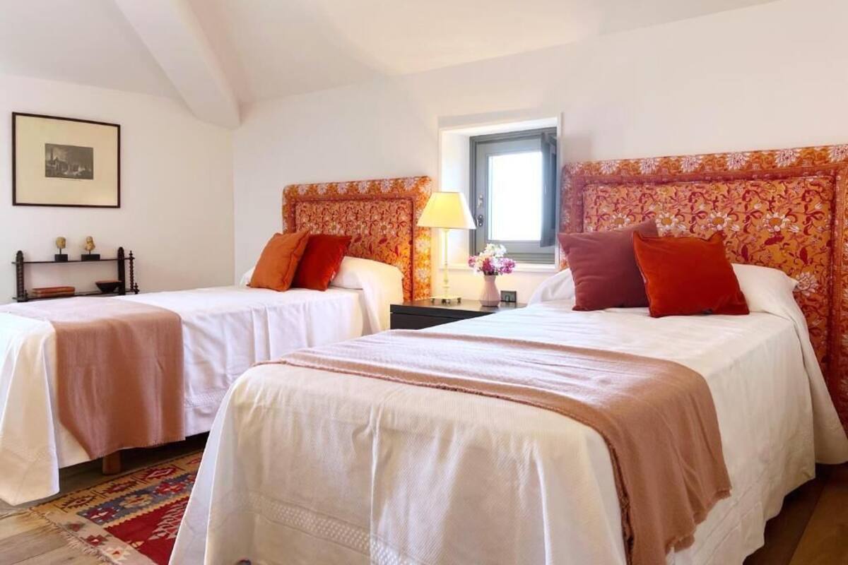 A hotel room with two beds, a window, a lamp, and a framed picture on the wall.
