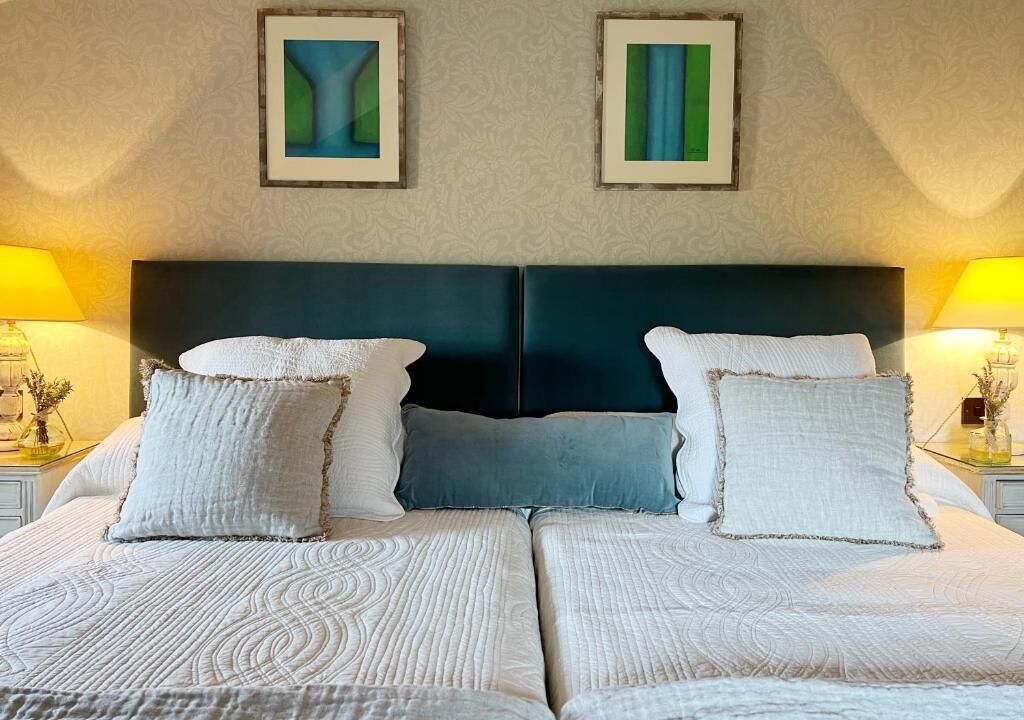 A double bed with a dark headboard, two bedside lamps, and two framed artworks on the wall.