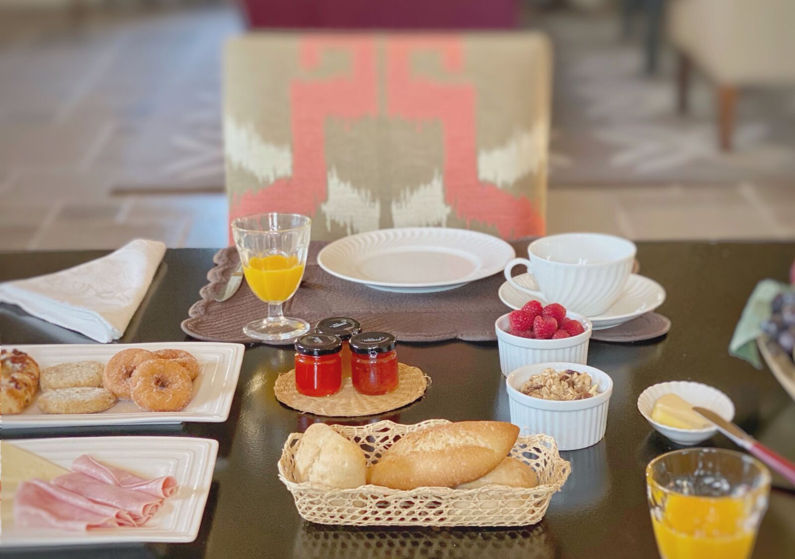 Una mesa de desayuno con platos de comida, un vaso de zumo de naranja y una cesta de pan.