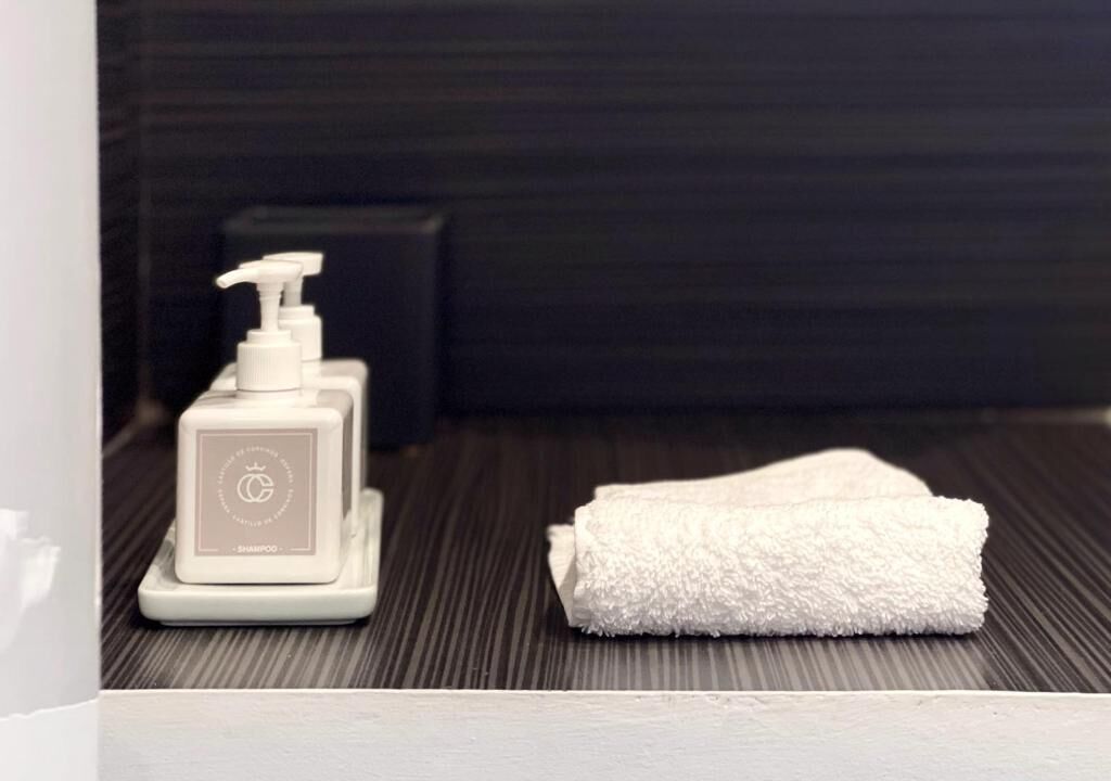 A bathroom with a white towel and a white bottle of shampoo on a textured floor.