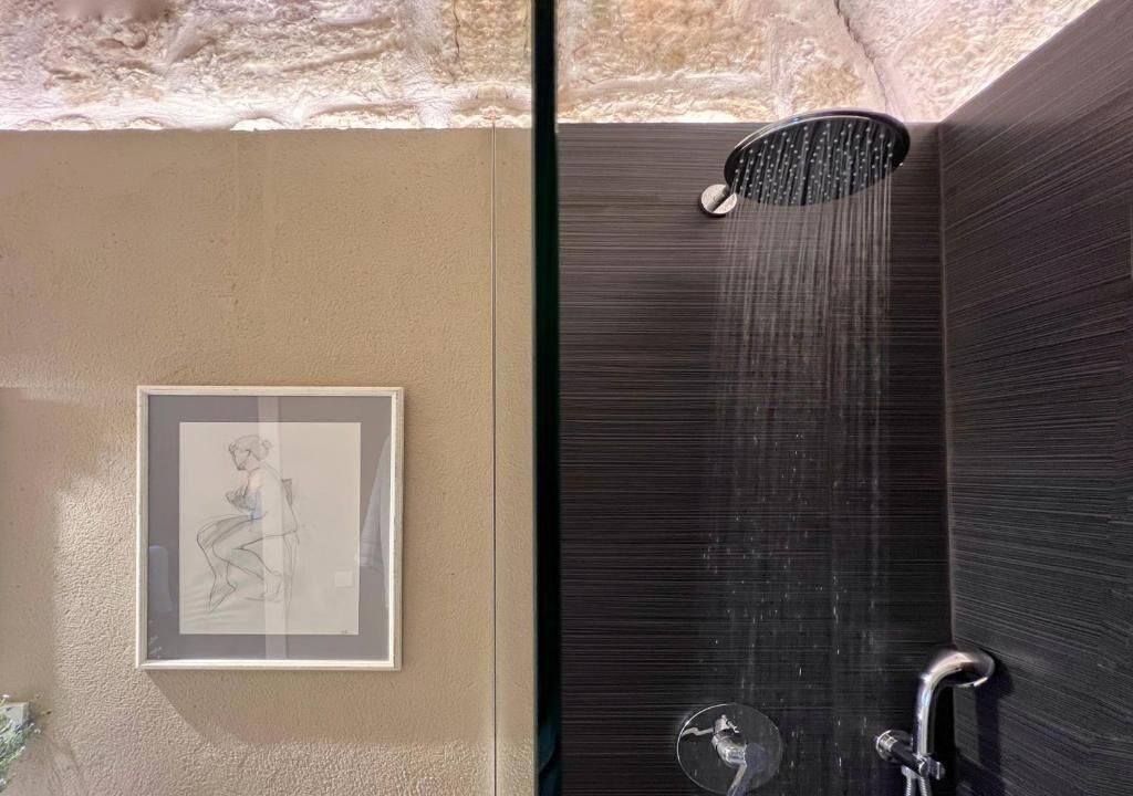 Une salle de bain avec une douche, une œuvre d’art encadrée et un mur à texture.