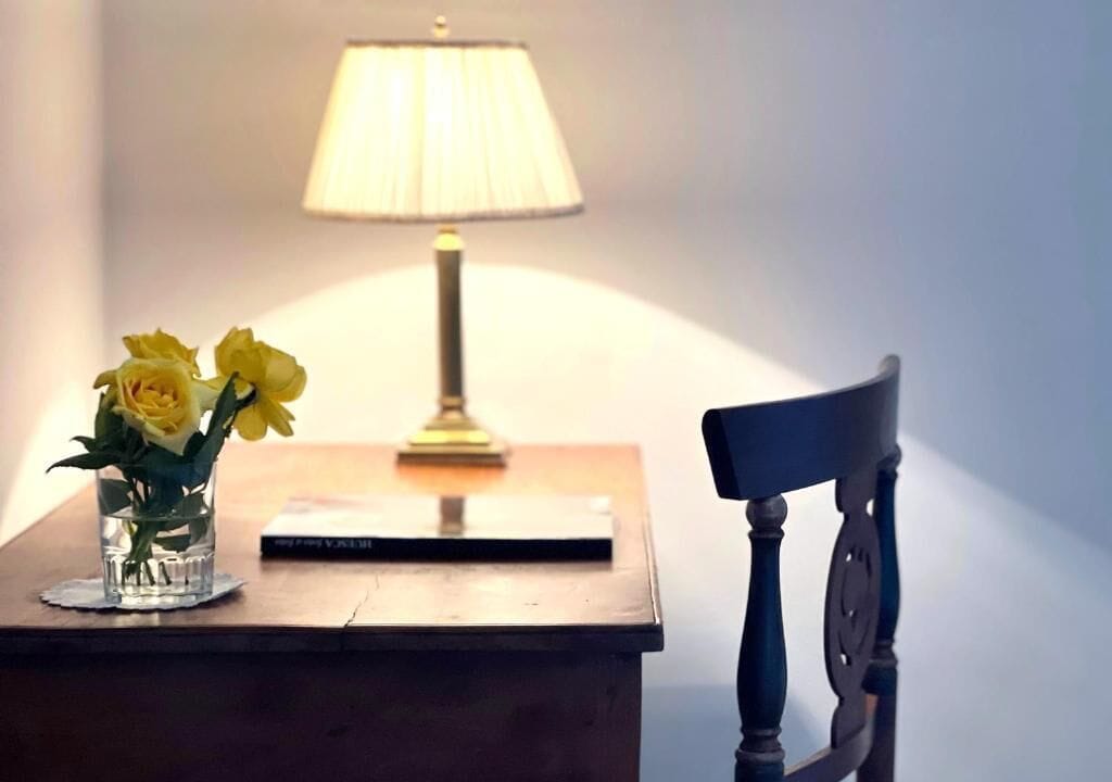 A desk with a lamp, a book, and a vase with flowers.