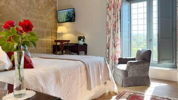 A bedroom with a bed, a desk, a chair, a vase with flowers, and a window with curtains.