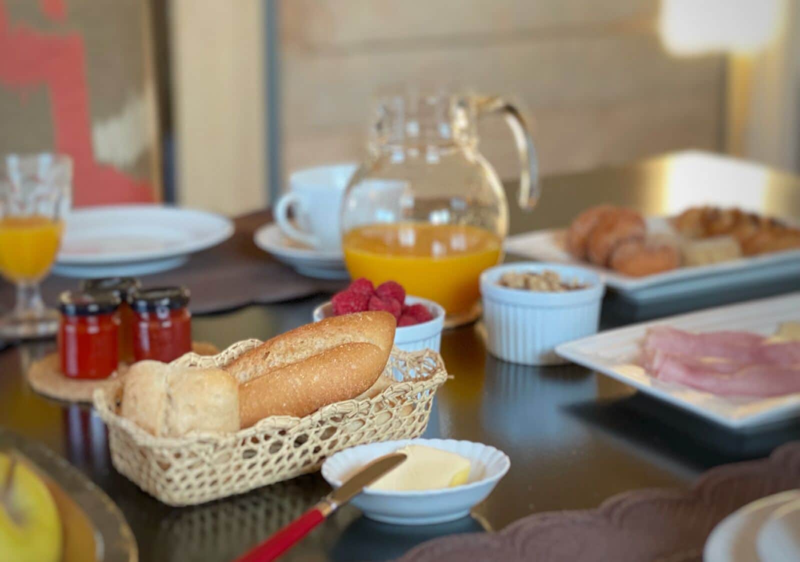 Un bufé de desayuno con pan, bollería y una jarra de zumo de naranja.