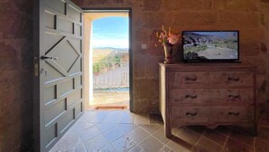 An open door leading to a balcony with a view, a wooden dresser with a television, and a vase with flowers. - Castillo de Corvinos (Albero Alto)