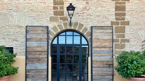 A building entrance with a wooden door, a stone wall, and a potted plant. - Castillo de Corvinos (Albero Alto)
