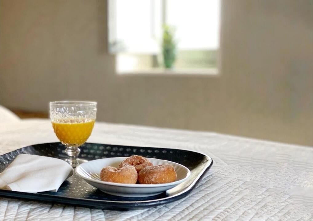 A tray with a glass of orange juice, a plate of doughnuts, and a napkin on a bed.