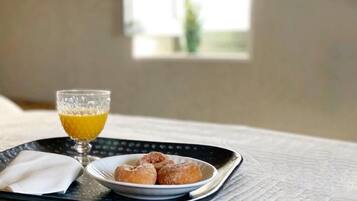 A tray with a glass of orange juice, a plate of doughnuts, and a napkin on a bed.