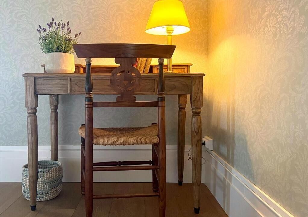 A wooden chair with a woven seat, a table with a lamp, and a potted plant.