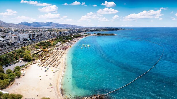 A coastal cityscape with a beach, clear blue waters, and a distant mountain range.