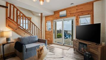 A living room with a wooden staircase, a grey sofa, a flat-screen TV, and a fireplace.