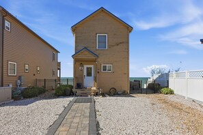 A two-story wooden building with a front door and a small porch, surrounded by gravel and a fence. - Twilight Tides-Lake Front/HotTub/6 Min GOTL Strip (Ashtabula)