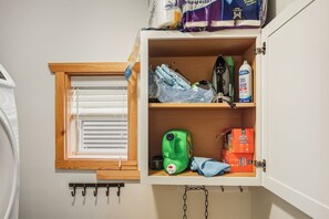 A storage cabinet with shelves containing cleaning supplies, a window with blinds, and a hook rack. - Twilight Tides-Lake Front/HotTub/6 Min GOTL Strip (Ashtabula)