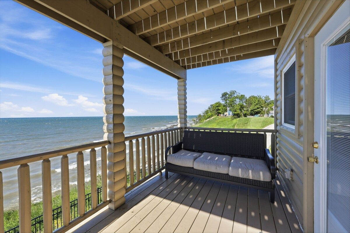 A covered porch with a bench, overlooking a body of water and a grassy area.