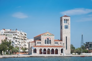 Une église dotée d’un haut clocher et d’une horloge, entourée de bâtiments modernes et située au bord de l’eau.