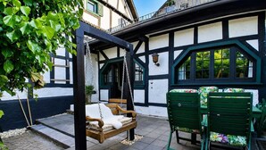 Eine Terrasse mit einer Schaukel, einem Tisch mit Stühlen und einem Gebäude mit freiliegenden Holzbalken.