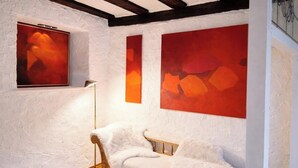 Ein Zimmer mit weißer Wand mit Struktur, einer Holzbodenverkleidung, einem weißen Sofa und abstrakten roten Gemälden.