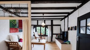 Ein Zimmer mit einer hölzernen Sitzbank, einem Tisch, einer Pendelleuchte und einem fenster mit Vorhängen.
