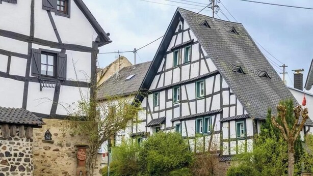 Ein traditionelles Fachwerkhäuschen mit steilem Dach, einer Steinwand und einem kleinen Garten.