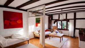 Ein Zimmer mit einem weißen Sofa, einem Holzstuhl, einem Tisch und einem roten, abstrakten Gemälde an der Wand.