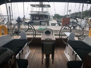 A boat's deck with two steering wheels, a control panel, and a view of other boats and a dock.