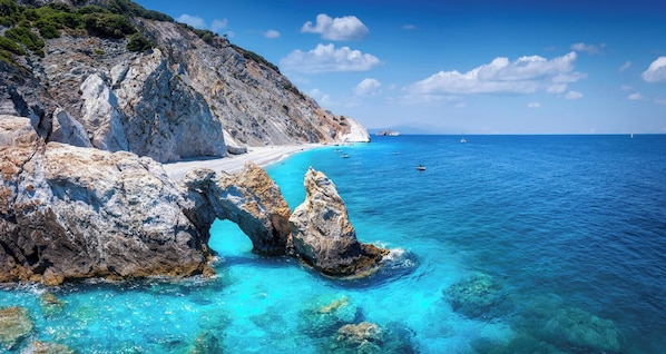 A coastal landscape with a prominent rock formation, clear turquoise waters, and a distant shoreline.