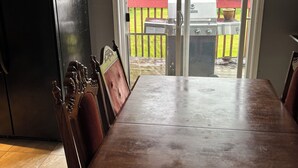 Ein Essbereich mit großem Tisch und Stühlen, einem schwarzen Kühlschrank und einer Glastür zum Außenbereich mit Grill.