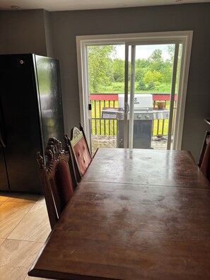 A dining area with a large table and chairs, a black refrigerator, and a sliding glass door leading to an outdoor patio with a grill. - Lodge Guest Country Home - Forest Bathers Delight. Close to Many trails! (Everett)