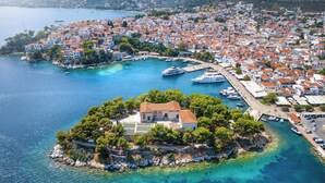 An aerial view of a coastal town with a prominent island featuring a large building surrounded by trees. - Sun-Kissed Sailing Adventure in Islas Esporadas (Skiathos)