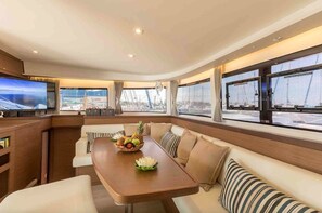 A modern interior with a wooden table, cushioned seating, and large windows offering a view of the sea.
