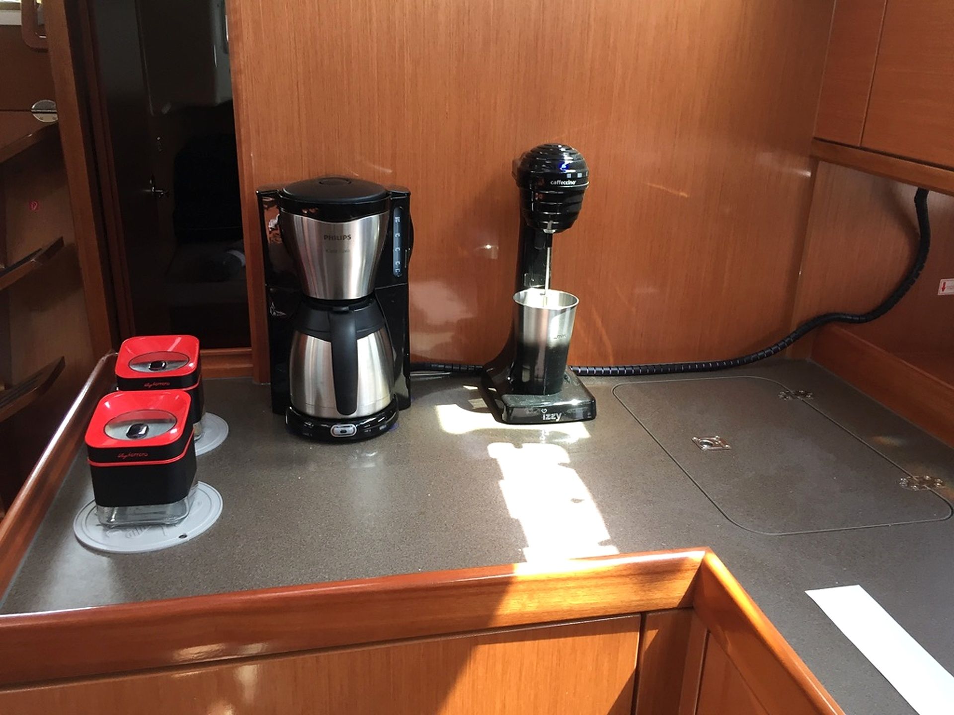 A kitchenette with a coffee maker, a kettle, and a red electric kettle on the counter.
