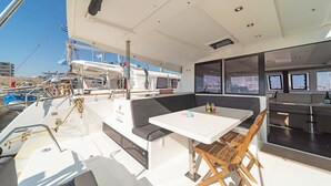 Le pont d’un bateau, avec une table, des sièges et une vue sur d’autres bateaux et des bâtiments.