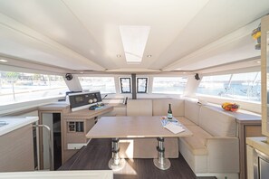 A boat's interior with a dining area, a control panel, and a view of the marina.