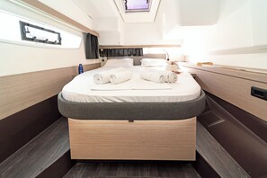 A compact, well-lit bedroom with a bed, pillows, a small bedside table, and a window.