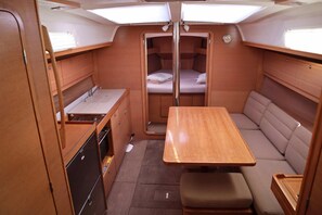 A compact RV interior with a kitchenette, a dining area, and a sleeping berth. - Sun-Kissed Sailing Adventure in Islas Sarónicas (Alimos)