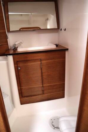 A compact bathroom with a wooden vanity, a mirror, and a toilet. - Sun-Kissed Sailing Adventure in Islas Sarónicas (Alimos)