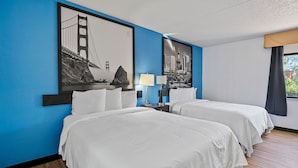A hotel room with two beds, a nightstand with a lamp, and two large wall art pieces depicting famous bridges.